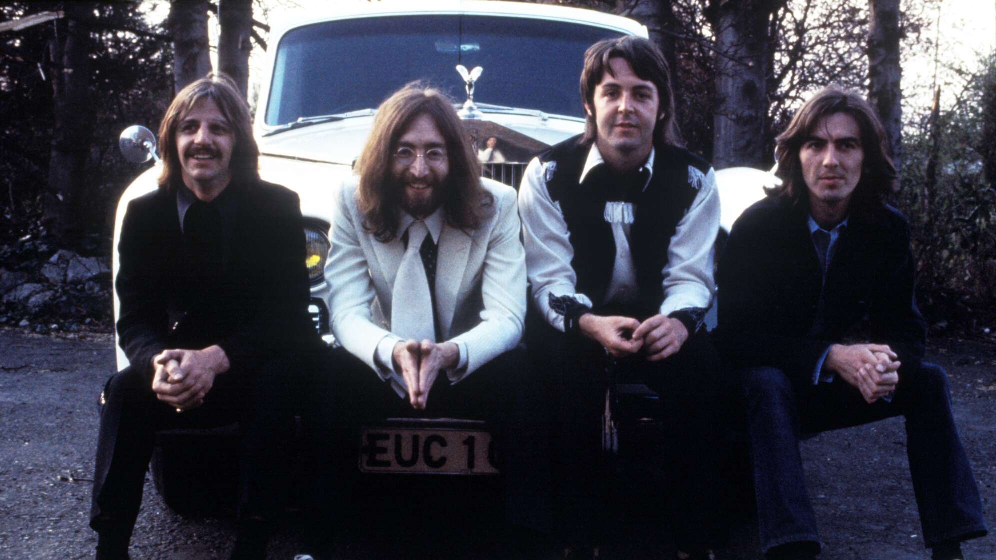 Die vier Beatles sitzen vor einem weißen Auto