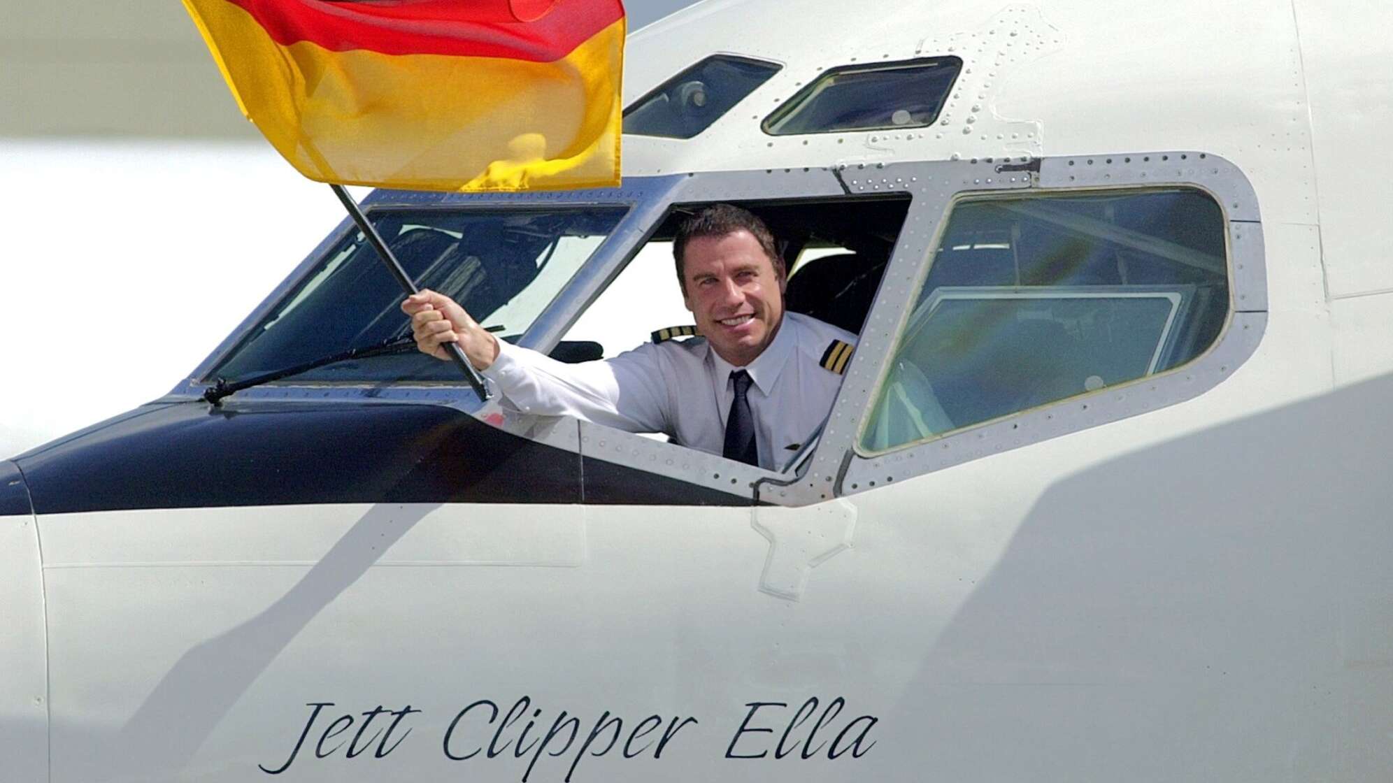 John Travolta schwenkt eine Deutschlandfahne aus dem Cockpit seines Flugzeugs